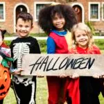 Children in Halloween costumes holding a Halloween sign