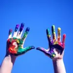 Two hands painted in bright colors held up against the sky