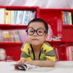A young boy reading a book in the classroom library corner